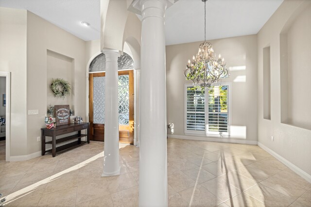 entryway featuring light tile patterned floors, ornate columns, and a notable chandelier