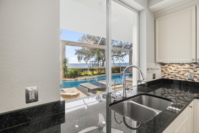 kitchen with white cabinets, backsplash, dark stone countertops, and sink