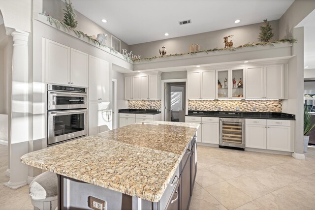 kitchen featuring a center island, light stone countertops, double oven, white cabinetry, and beverage cooler