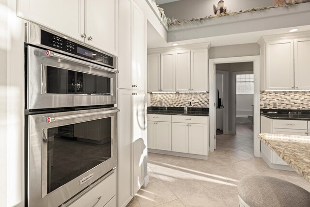 kitchen with tasteful backsplash, white cabinetry, light tile patterned floors, and stainless steel double oven