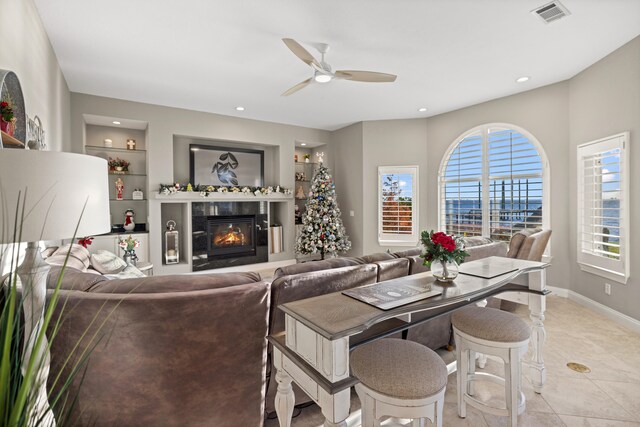 tiled living room with a wealth of natural light, built in features, and ceiling fan