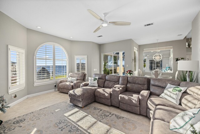 tiled living room with ceiling fan with notable chandelier