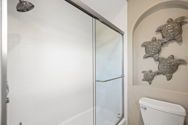 bathroom featuring combined bath / shower with glass door and toilet