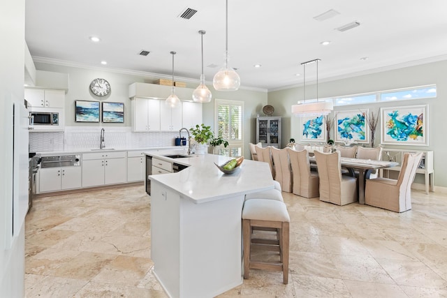 kitchen featuring stainless steel microwave, sink, pendant lighting, decorative backsplash, and white cabinets