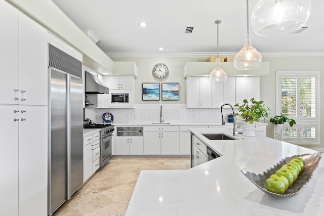 kitchen featuring sink, wall chimney range hood, built in appliances, pendant lighting, and white cabinets