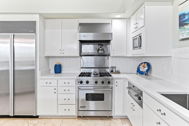 kitchen with white cabinets, decorative backsplash, built in appliances, and wall chimney exhaust hood