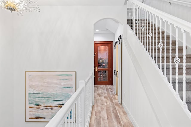 staircase with a barn door, wood-type flooring, and an inviting chandelier