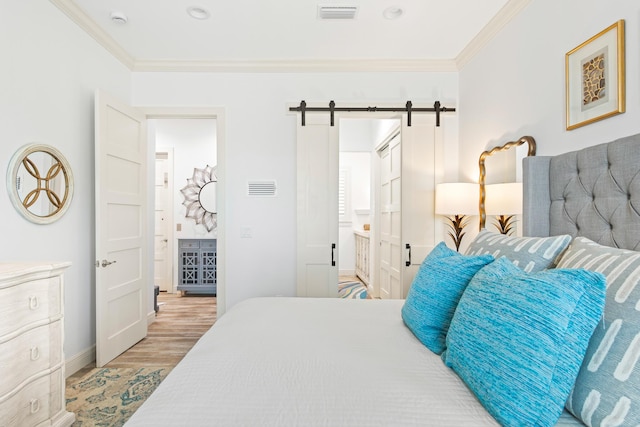 bedroom featuring a barn door, crown molding, connected bathroom, and light hardwood / wood-style flooring