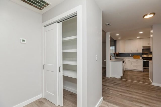 interior space with light wood-type flooring, stainless steel stove, white cabinetry, and sink