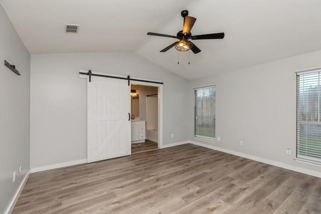 empty room with a barn door, ceiling fan, light hardwood / wood-style floors, and vaulted ceiling