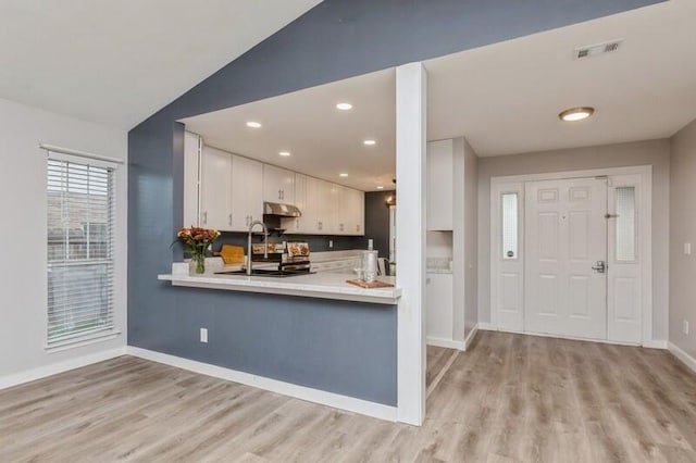 kitchen with sink, light hardwood / wood-style flooring, kitchen peninsula, lofted ceiling, and white cabinets