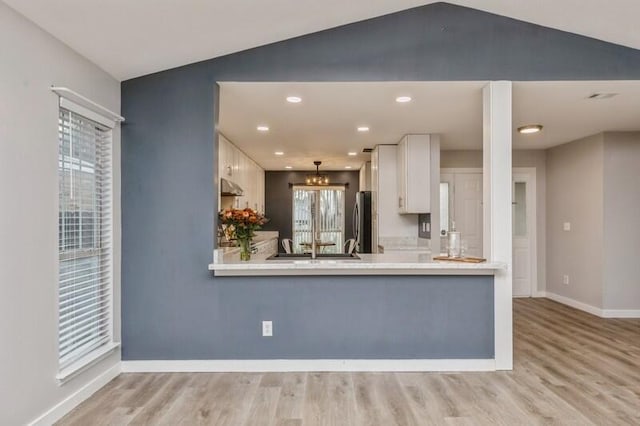 kitchen with white cabinets, light wood-type flooring, stainless steel refrigerator, and lofted ceiling