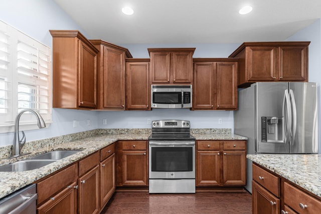 kitchen with appliances with stainless steel finishes, light stone counters, dark wood-type flooring, and sink