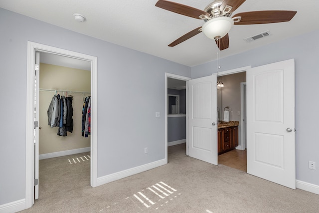 unfurnished bedroom with a walk in closet, ceiling fan, ensuite bathroom, and light colored carpet