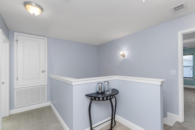 hall featuring light carpet and a textured ceiling