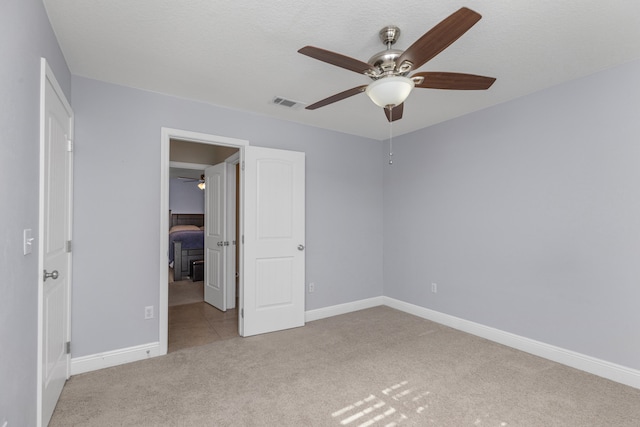 unfurnished bedroom featuring ceiling fan, light colored carpet, and a textured ceiling