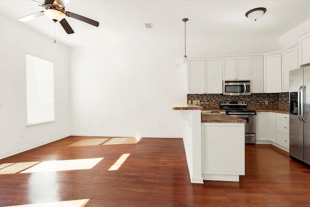 kitchen with appliances with stainless steel finishes, hanging light fixtures, dark hardwood / wood-style floors, white cabinets, and decorative backsplash