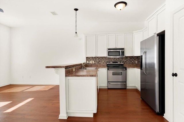 kitchen with stainless steel appliances, kitchen peninsula, hanging light fixtures, and white cabinets