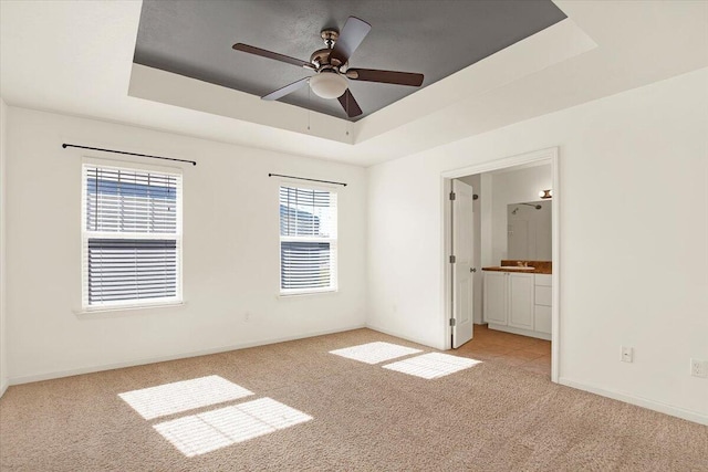 unfurnished bedroom featuring ceiling fan, connected bathroom, a raised ceiling, and light carpet