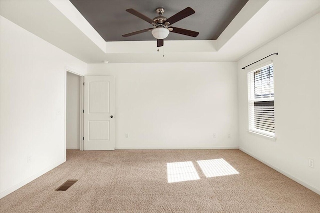 empty room featuring ceiling fan, light colored carpet, and a tray ceiling