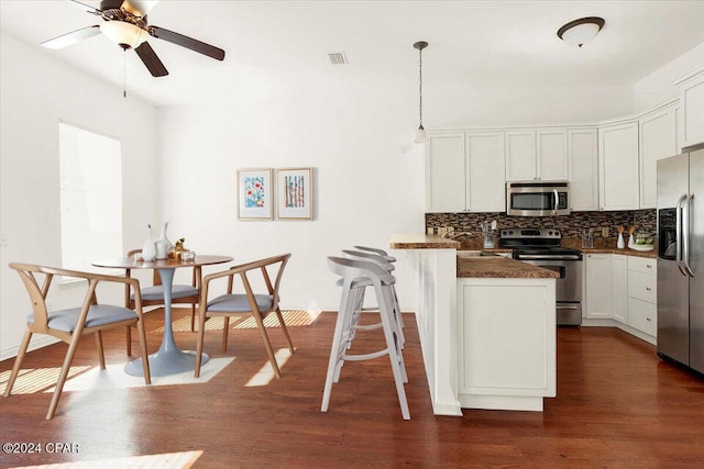 kitchen with dark wood-type flooring, white cabinetry, backsplash, stainless steel appliances, and decorative light fixtures