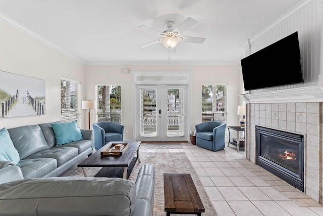 living room with a tile fireplace, ceiling fan, french doors, crown molding, and light tile patterned flooring