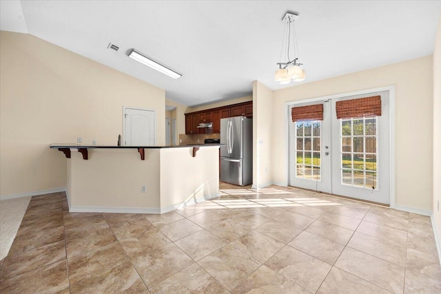 kitchen featuring stainless steel fridge, lofted ceiling, a breakfast bar area, and hanging light fixtures