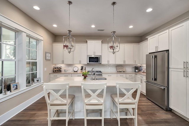 kitchen featuring pendant lighting, stainless steel appliances, white cabinetry, and a kitchen island with sink