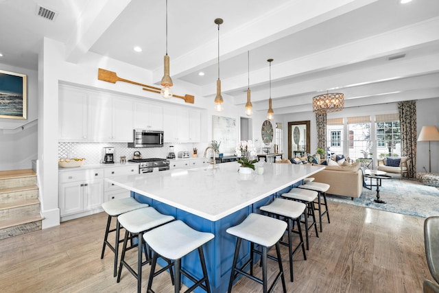 kitchen with appliances with stainless steel finishes, white cabinetry, pendant lighting, and beam ceiling