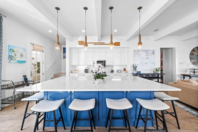 kitchen with beamed ceiling, light wood-type flooring, decorative light fixtures, and white cabinetry