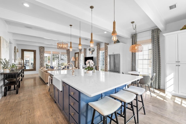 kitchen featuring white cabinetry, sink, beamed ceiling, light hardwood / wood-style floors, and decorative light fixtures