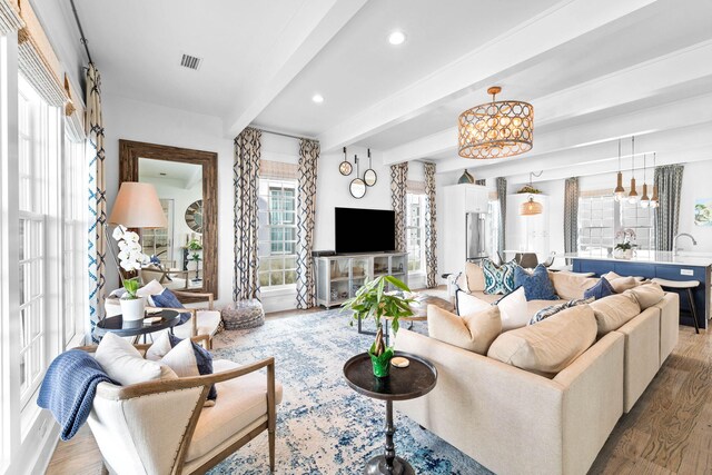 living room with beamed ceiling, wood-type flooring, an inviting chandelier, and sink