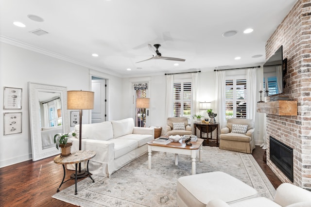 living room featuring hardwood / wood-style floors, ceiling fan, ornamental molding, and a brick fireplace