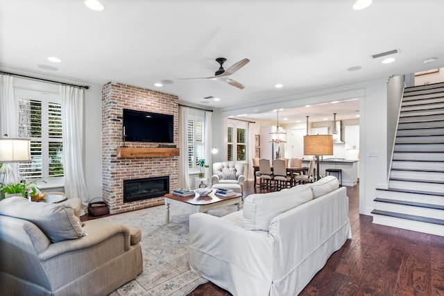 living room with a fireplace, ceiling fan, and dark wood-type flooring