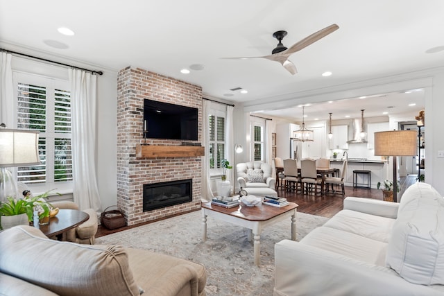 living room with wood-type flooring, ceiling fan with notable chandelier, and a brick fireplace