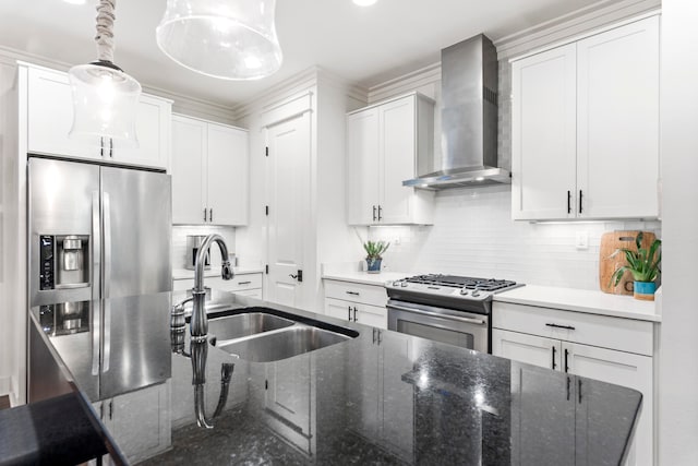 kitchen with appliances with stainless steel finishes, wall chimney exhaust hood, dark stone countertops, white cabinets, and hanging light fixtures