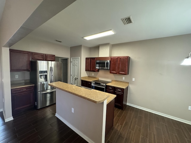 kitchen with a kitchen island with sink, dark wood-type flooring, and stainless steel appliances