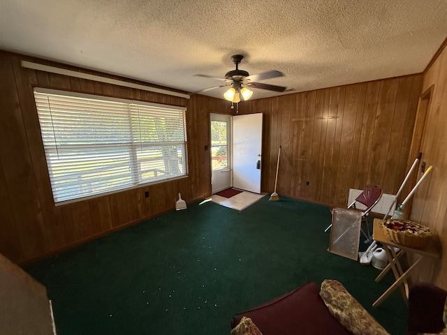 sitting room with wooden walls, carpet, a textured ceiling, and ceiling fan