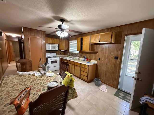 kitchen featuring a textured ceiling, white appliances, ceiling fan, sink, and wood walls