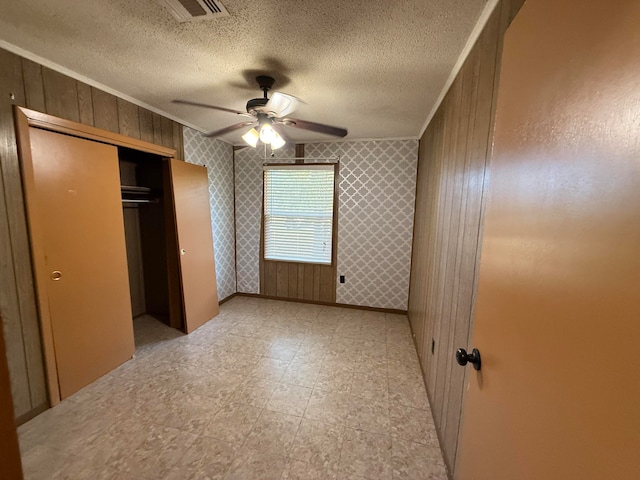 unfurnished bedroom featuring a textured ceiling, a closet, ceiling fan, and wood walls