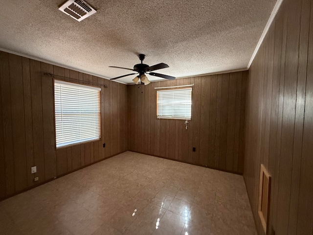 spare room featuring ceiling fan, wood walls, and a textured ceiling