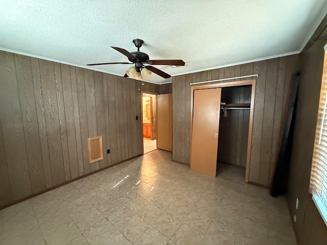 unfurnished bedroom featuring ceiling fan, wooden walls, and a closet