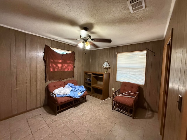 sitting room featuring wooden walls, ceiling fan, and a textured ceiling