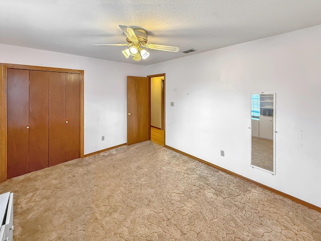 unfurnished bedroom with light carpet, ceiling fan, a closet, and a textured ceiling