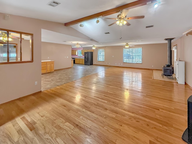 unfurnished living room featuring ceiling fan, vaulted ceiling with beams, a wood stove, and light wood-type flooring