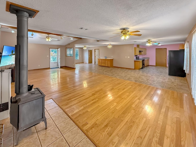 unfurnished living room with lofted ceiling, light hardwood / wood-style floors, a textured ceiling, and a wood stove