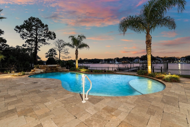 pool at dusk featuring a water view and a patio