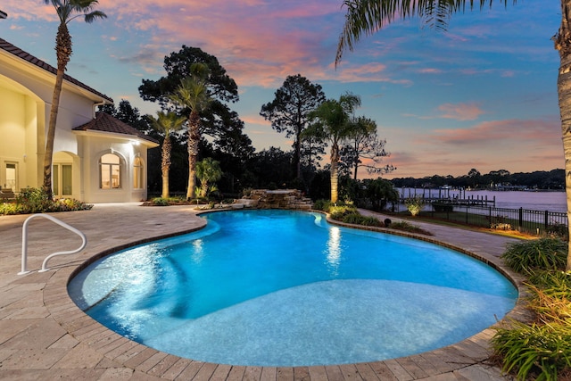 pool at dusk featuring a water view and a patio