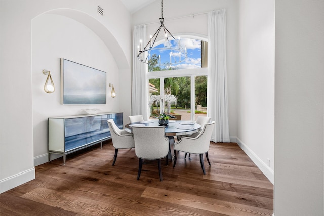 dining space featuring wood-type flooring, vaulted ceiling, and an inviting chandelier