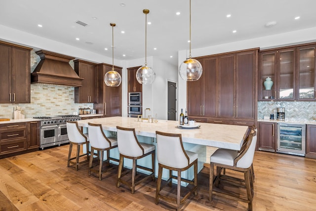 kitchen with wine cooler, light wood-type flooring, premium range hood, and appliances with stainless steel finishes